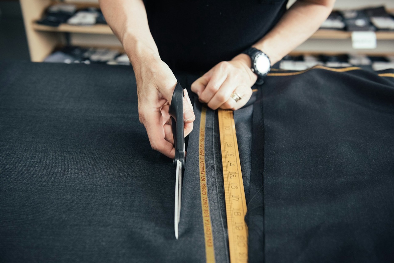 A tailor cutting cloth with shears and a tape measure